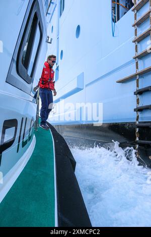 Nice, France : bateau pilote portuaire approchant l'HYMNE DES MERS géant de Royal Caribbean pour embarquer le pilote maritime à Villefranche sur mer. Une escale unique pour le plus grand bateau de croisière cette année dans le petit port de la Côte d'Azur. Après la saison estivale, l'impressionnant navire devait naviguer à travers le canal de Suez dans le cadre d'un repositionnement de l'Europe vers un nouveau port d'attache à Singapour, mais à la suite des tensions de la mer Rouge et des menaces d'attaques de missiles Houthi sur les navires, il transportera plutôt sans passager autour de la pointe sud de l'Afrique pour rejoindre Dubaï et l'Asie. Crédit : Kevin Izorce/Alamy Live News Banque D'Images