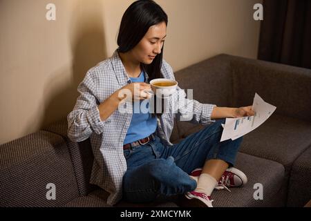 Femme asiatique assise sur un canapé et regardant à travers des papiers avec des graphiques Banque D'Images
