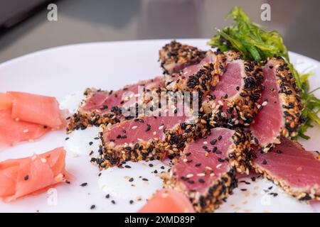 Une assiette de nourriture avec un morceau de thon finement tranché et quelques graines de sésame sur le dessus. L'assiette est blanche et la nourriture est disposée dans un m visuellement attrayant Banque D'Images