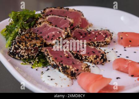 Une assiette de nourriture avec un morceau de thon finement tranché et quelques graines de sésame sur le dessus. L'assiette est blanche et la nourriture est disposée dans un m visuellement attrayant Banque D'Images