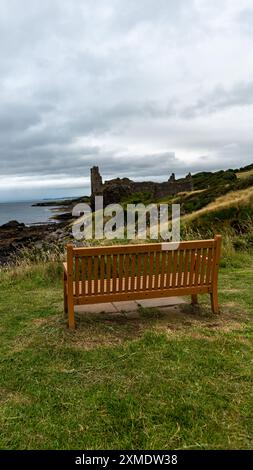 Banc vide se trouve sur une colline surplombant les ruines d'un château médiéval par un jour nuageux en écosse Banque D'Images