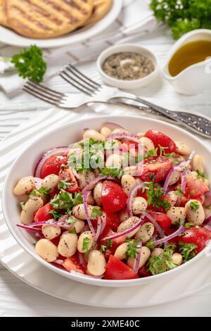 Piyaz, salade de haricots blancs turcs avec tomates, oignon rouge, persil, aromatisée au sumac et vinaigrette à l'huile d'olive dans un bol sur une table en bois blanc avec fourchette Banque D'Images