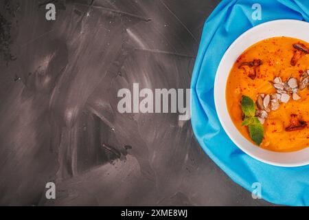 Soupe de purée de citrouille avec des graines et des champignons chanterelles sur un fond texturé gris avec une serviette bleue et faux. Placer pour le texte. Presentation exquise Banque D'Images