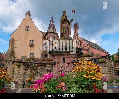 La fontaine du… Léon sur la place Saint-Léon au centre d'Eguisheim en Alsace. Des maisons à colombages bien entretenues et des décorations florales caractérisent Banque D'Images