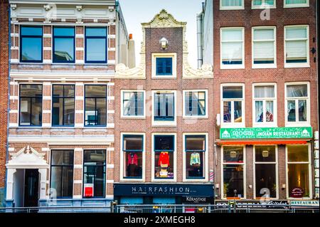 À Amsterdam, une rangée vibrante de bâtiments en briques colorés borde la rue. Des entreprises comme des salons de coiffure, des restaurants et des boutiques de cadeaux remplissent le sol flo Banque D'Images