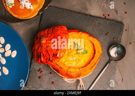 Citrouille cuite farcie de purée de légumes avec des champignons chanterelles sur un tableau noir et une assiette bleue avec des graines de citrouille. Photo de haute qualité Banque D'Images