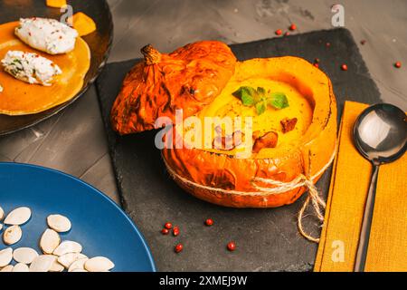 Citrouille cuite farcie de purée de légumes avec des champignons chanterelles sur un tableau noir et une assiette bleue avec des graines de citrouille. Photo de haute qualité Banque D'Images