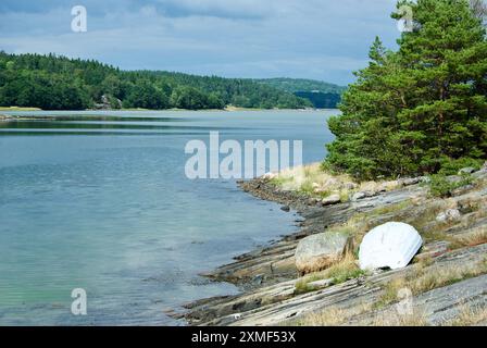 Paysage côtier avec un bateau blanc couché à l'envers sur un rocher de baignade sur la côte ouest suédoise en été. Banque D'Images