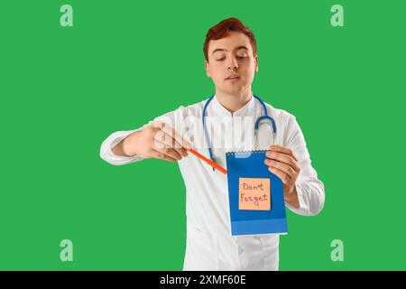 Médecin masculin pointant sur le cahier avec le texte NE PAS OUBLIER sur fond vert Banque D'Images