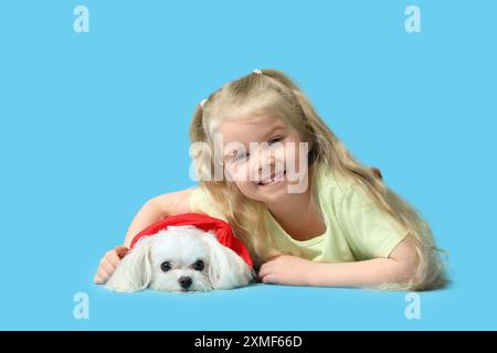 Mignonne petite fille avec chien maltais couché sur fond bleu Banque D'Images