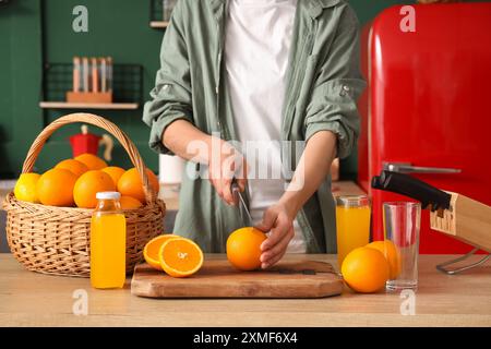 Jeune femme coupant l'orange près du panier en osier avec des agrumes dans la cuisine verte Banque D'Images