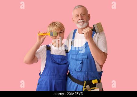 Couple mature de décorateurs avec des pinceaux sur fond rose Banque D'Images