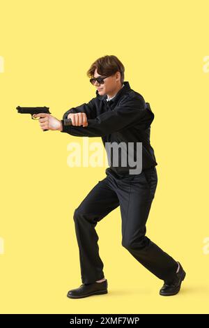 Garde de sécurité masculin avec arme à feu et lampe de poche sur fond jaune Banque D'Images