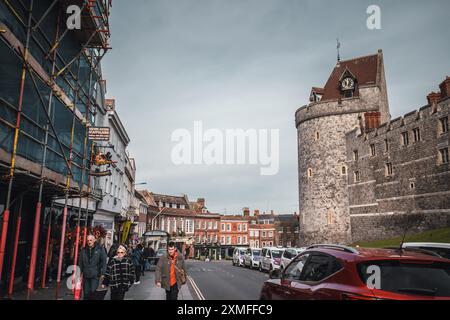 Windor Castle, Royaume-Uni - 16 octobre 2023 : Une vue en bas d'une rue bordée de bâtiments, vers une grande tour en pierre avec une horloge. Les voitures sont garées le long du s. Banque D'Images