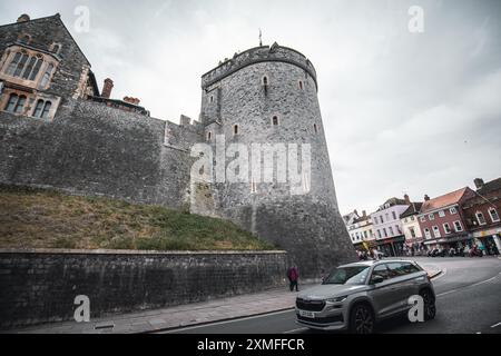 Windor Castle, Royaume-Uni - 16 octobre 2023 : Une tour de pierre s'élève au-dessus d'un mur de pierre épais, avec une voiture moderne garée dans la rue ci-dessous. Banque D'Images