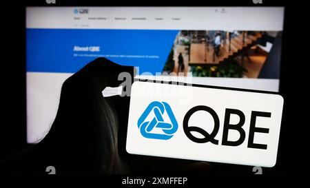 Personne tenant un smartphone avec le logo de la société australienne QBE Insurance Group Limited devant le site Web. Concentrez-vous sur l'affichage du téléphone. Banque D'Images