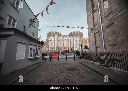 Château de Windor, Royaume-Uni - 16 octobre 2023 : Une rue pavée mène à l'entrée d'un château de pierre, avec une chaîne de drapeaux britanniques suspendus au-dessus. Banque D'Images