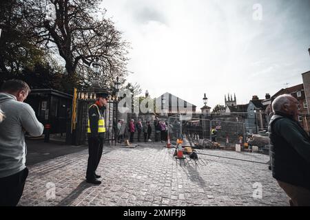 Château de Windor, Royaume-Uni - 16 octobre 2023 : Un garde de sécurité se tient près d'une porte avec des gens qui l'attendent derrière lui. Rue pavée devant lui avec con Banque D'Images