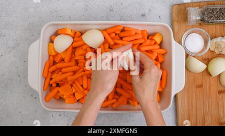 Recette de soupe de courge butternut rôtie. Gros plan des cubes de courge pelés et sans pépins, de la carotte, de l'oignon, de l'ail et des épices dans un plat en céramique sur le kit Banque D'Images