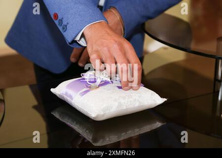 Le marié dans la veste bleue prend l'anneau de mariage du coussin d'anneau de mariage. Banque D'Images