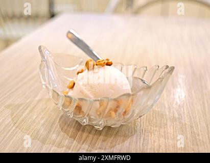 La crème glacée à la noix de coco circulaire avec des noix et une cuillère à l'intérieur du bol de dessert sucré en verre Banque D'Images