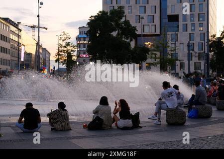 Besucher am Stachus Brunnen in Abendlicht Besucher sitzen am Stachus Brunnen auf dem Karlsplatz und sehen dem Wasserspiel zu oder unterhalten sich. Donc Banque D'Images