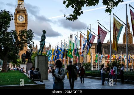 Les touristes marchent sur Parliament Square en face de Westminster et Big Ben tandis que les drapeaux du Commonwealth se balancent sur les mâts. Banque D'Images