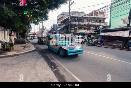 Manille, Philippines - 26 août 2019 : un jeepney dynamique conduit le long d'une rue animée remplie de boutiques et de piétons. Banque D'Images