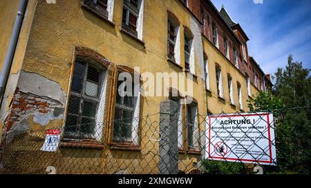 Perleberg, Allemagne. 25 juillet 2024. Un panneau sur une clôture à la caserne impériale dit "attention! Pas d'intrusion ni de conduite ! » est attaché à une clôture à la caserne impériale. Autrefois un «lieu perdu» et une beauté endormie, ils doivent maintenant être rénovés et convertis en bâtiments résidentiels et commerciaux. Il y a sept bâtiments de caserne avec environ 10 000 mètres carrés d'espace utilisable crédit : Jens Kalaene/dpa/Alamy Live News Banque D'Images