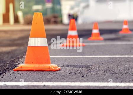 Vue rapprochée de cônes orange alignés sur une route asphaltée, indiquant une zone de construction ou d'entretien. Banque D'Images