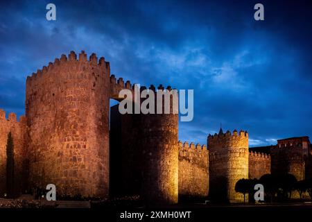 Vue nocturne de Puerta del Alcazar aux murs illuminés de la ville d'Avila à Castilla y Leon, Espagne. Architecture historique contre un ciel nocturne dramatique. Banque D'Images