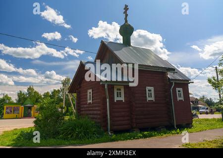 Une petite chapelle traditionnelle en bois avec un dôme vert et une croix située dans un village rural. La chapelle est entourée de verdure et placée contre un bri Banque D'Images