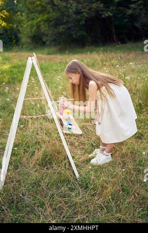 fille pré-adolescente dans une robe d'été peint une image dans le jardin sur un chevalet Banque D'Images