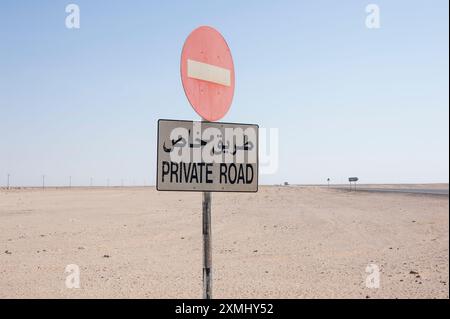 Route privée dans le désert d'Oman avec panneaux d'interdiction d'entrée et panneaux d'information bilingues, arabe et anglais Banque D'Images