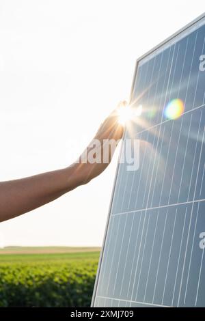 Gros plan d'une main touchant un panneau solaire au coucher du soleil. Banque D'Images