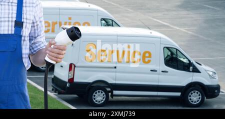 Un homme tient la prise de charge du véhicule électrique. Fourgonnettes électriques en arrière-plan. Banque D'Images