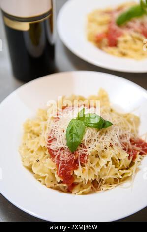 Un gros plan de pâtes italiennes garnies de sauce tomate, de fromage râpé et de feuilles de basilic frais, servies dans des assiettes blanches. Banque D'Images