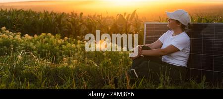 Femme portant un chapeau blanc est assis à côté du panneau solaire au coucher du soleil. Banque D'Images