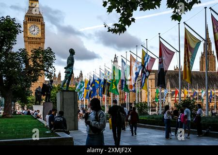 Les touristes marchent sur Parliament Square en face de Westminster et Big Ben tandis que les drapeaux du Commonwealth se balancent sur les mâts. Banque D'Images