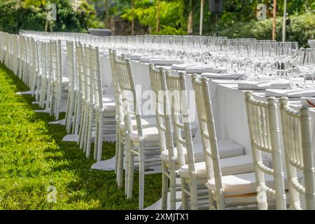Table de mariage servie avec assiettes, chaises blanches, serviettes et verres à vin Banque D'Images