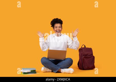 Excité jeune femme assise avec ordinateur portable et sac à dos sur jaune Banque D'Images