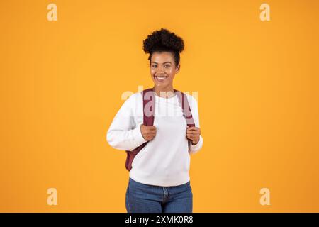 Heureuse jeune femme avec sac à dos debout devant jaune Banque D'Images