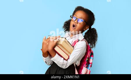 Fille d'école noire bâillant des livres posant sur fond jaune, Panorama Banque D'Images