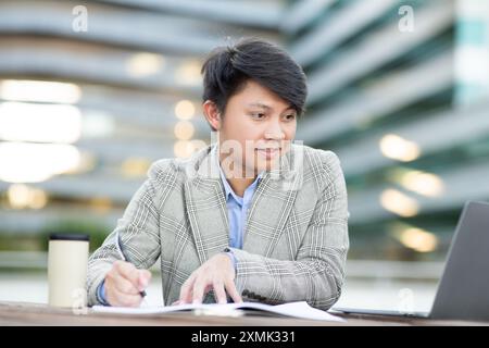 Jeune homme travaillant sur un ordinateur portable à l'extérieur de l'immeuble de bureaux Banque D'Images