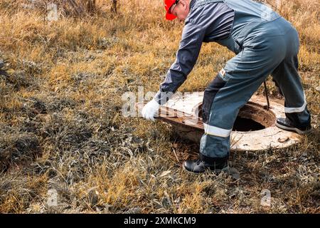 Un travailleur dans un casque ouvre le couvercle de trou d'homme pour entretenir un puits, espace de copie. Plomberie et égouts. Banque D'Images