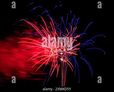 Exposition temporelle de feux d'artifice rouges blancs et bleus avec nuage de fumée se déplaçant en arrière-plan pendant l'affichage du 4 juillet Banque D'Images