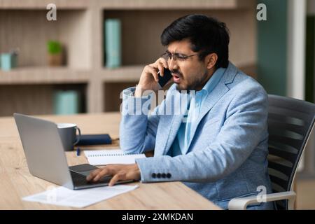 Homme d'affaires stressé parlant au téléphone tout en travaillant sur son ordinateur portable Banque D'Images