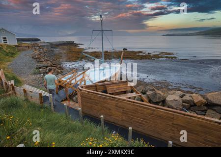 Homme marchant vers le jacuzzi en forme de bateau sur la côte islandaise au coucher du soleil Banque D'Images