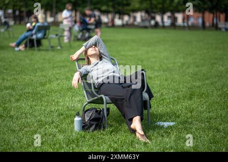 Femme fatiguée de travail prendre pause détendue s'incline sur la chaise dans l'espace public ouvert sur la pelouse mains sur les yeux. Banque D'Images