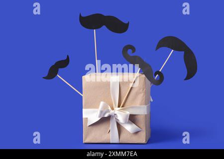 Boîte cadeau avec différentes moustaches en papier sur fond bleu Banque D'Images